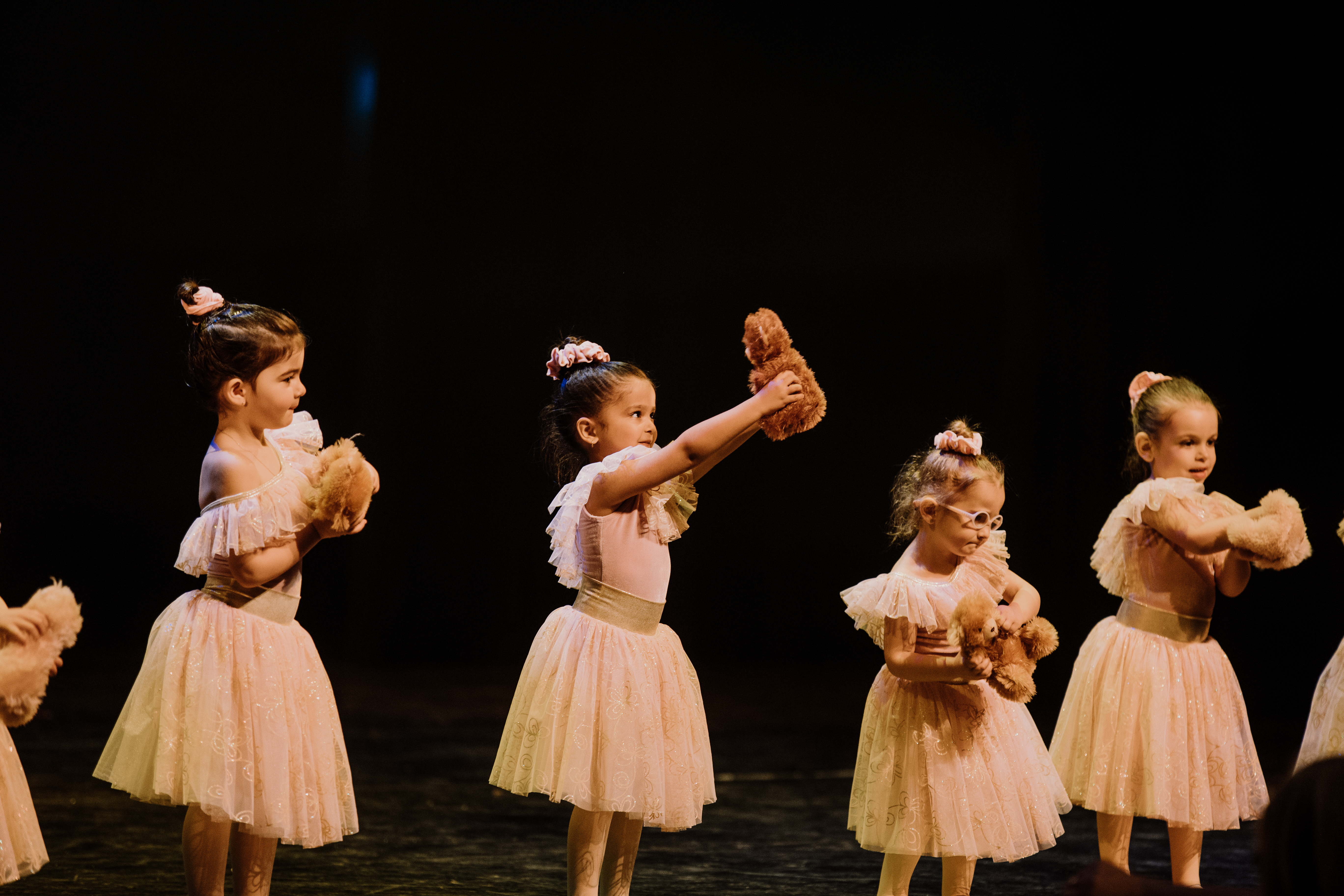 Four dancers holding teddy bears on stage during a ballet routine