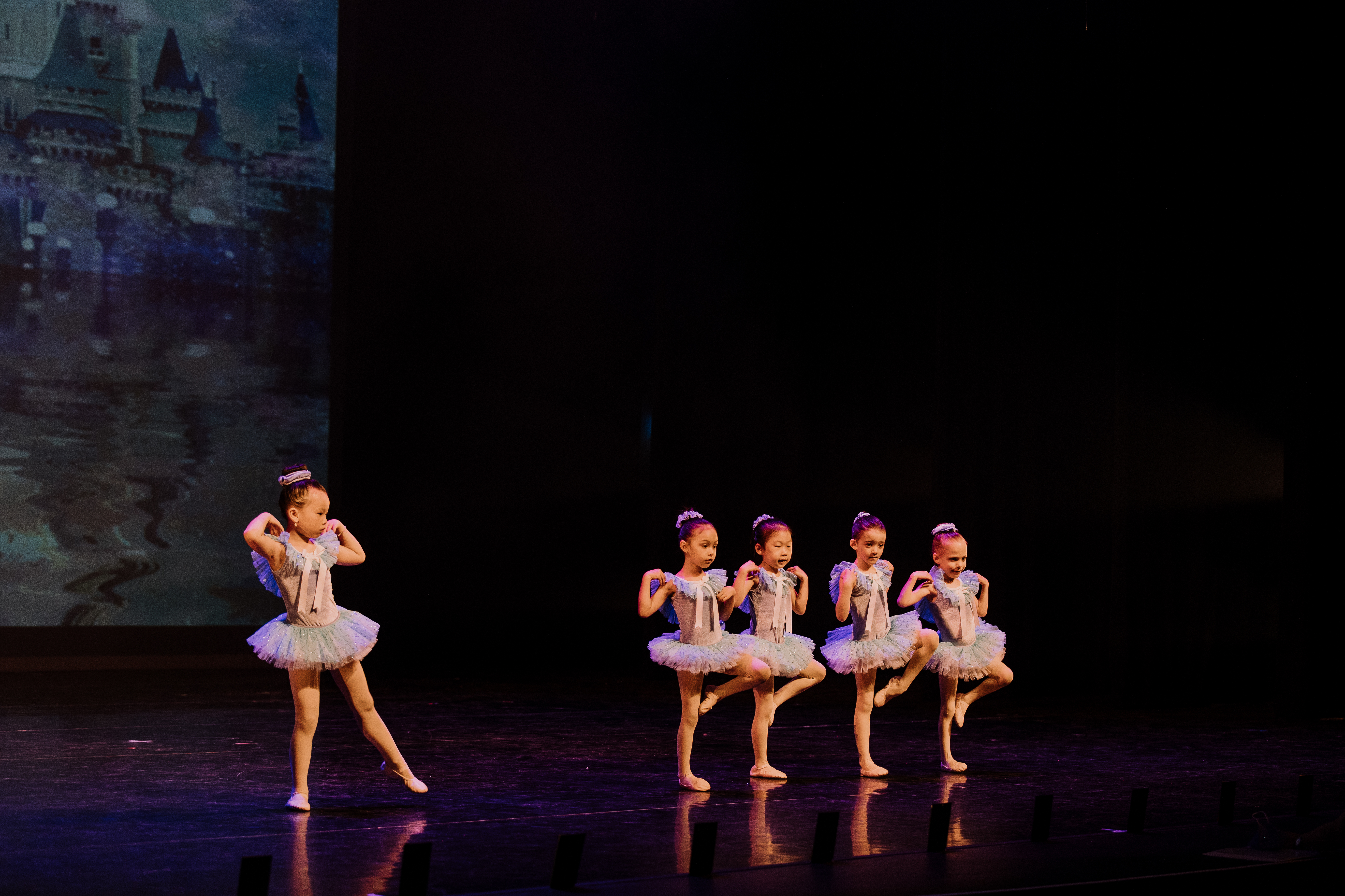 Five dancers performing a ballet routine on stage in blue tutus