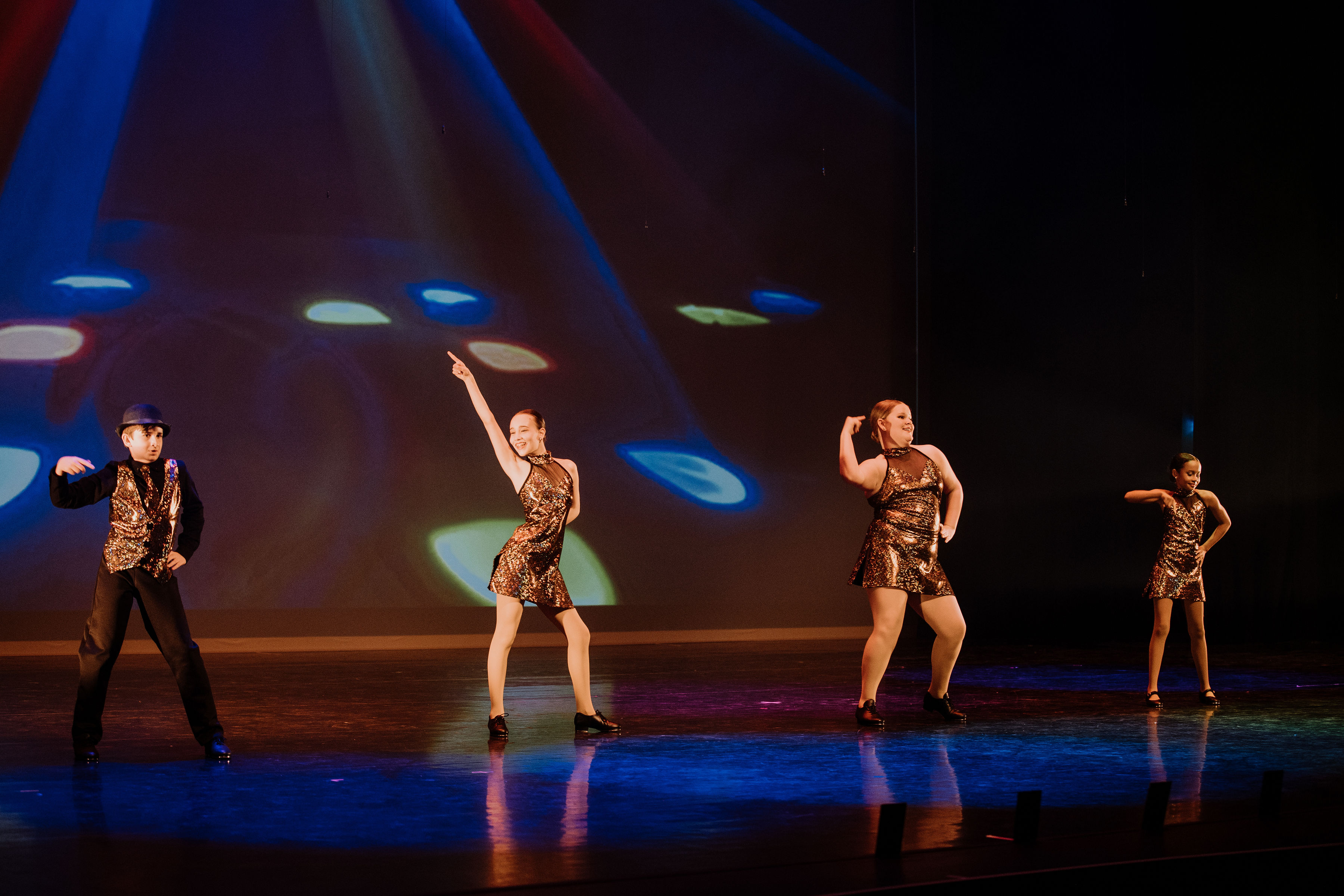 Four tap dancers doing a disco move during their on stage performance