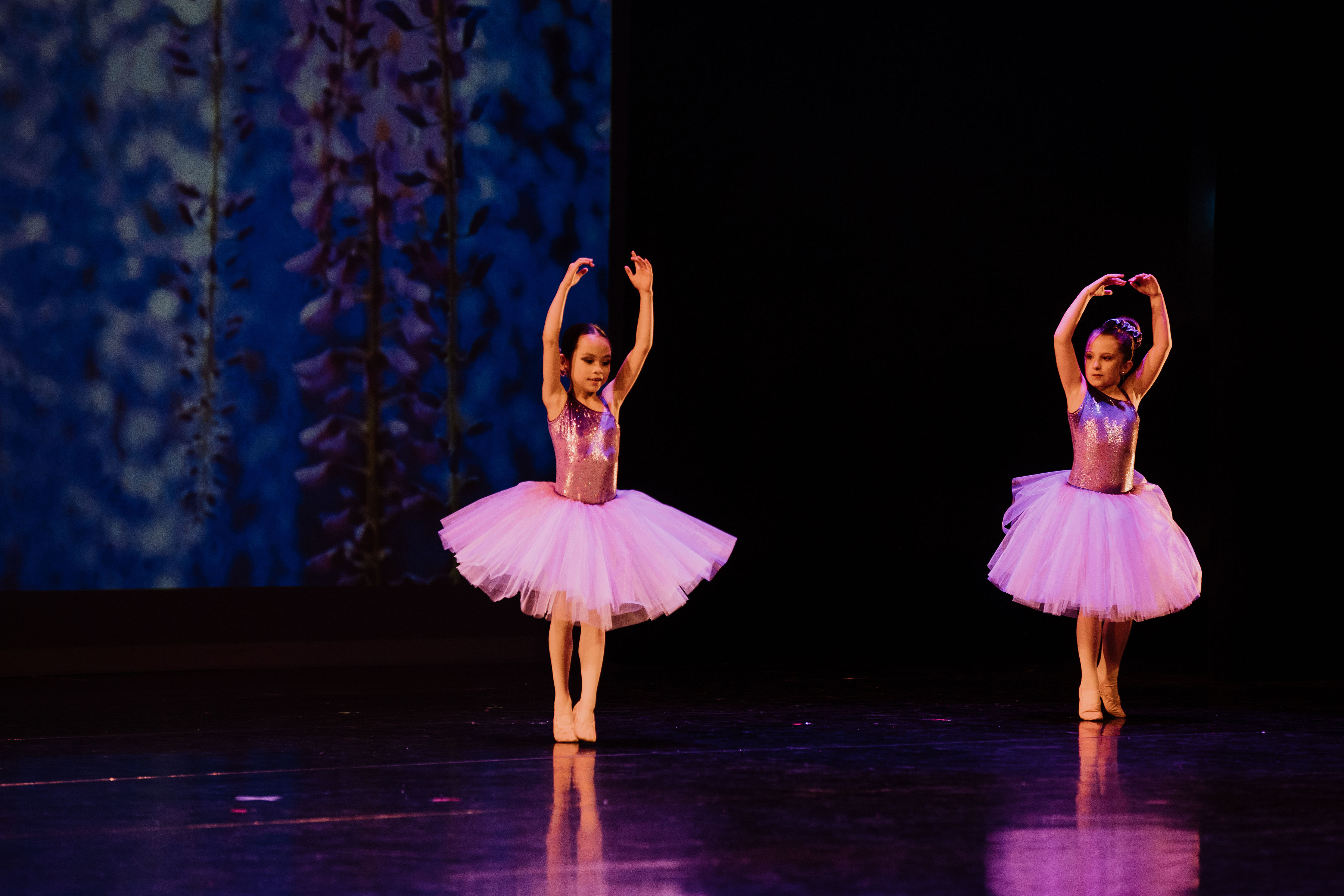Two dancers with their arms in fifth in sparkly pink tutus