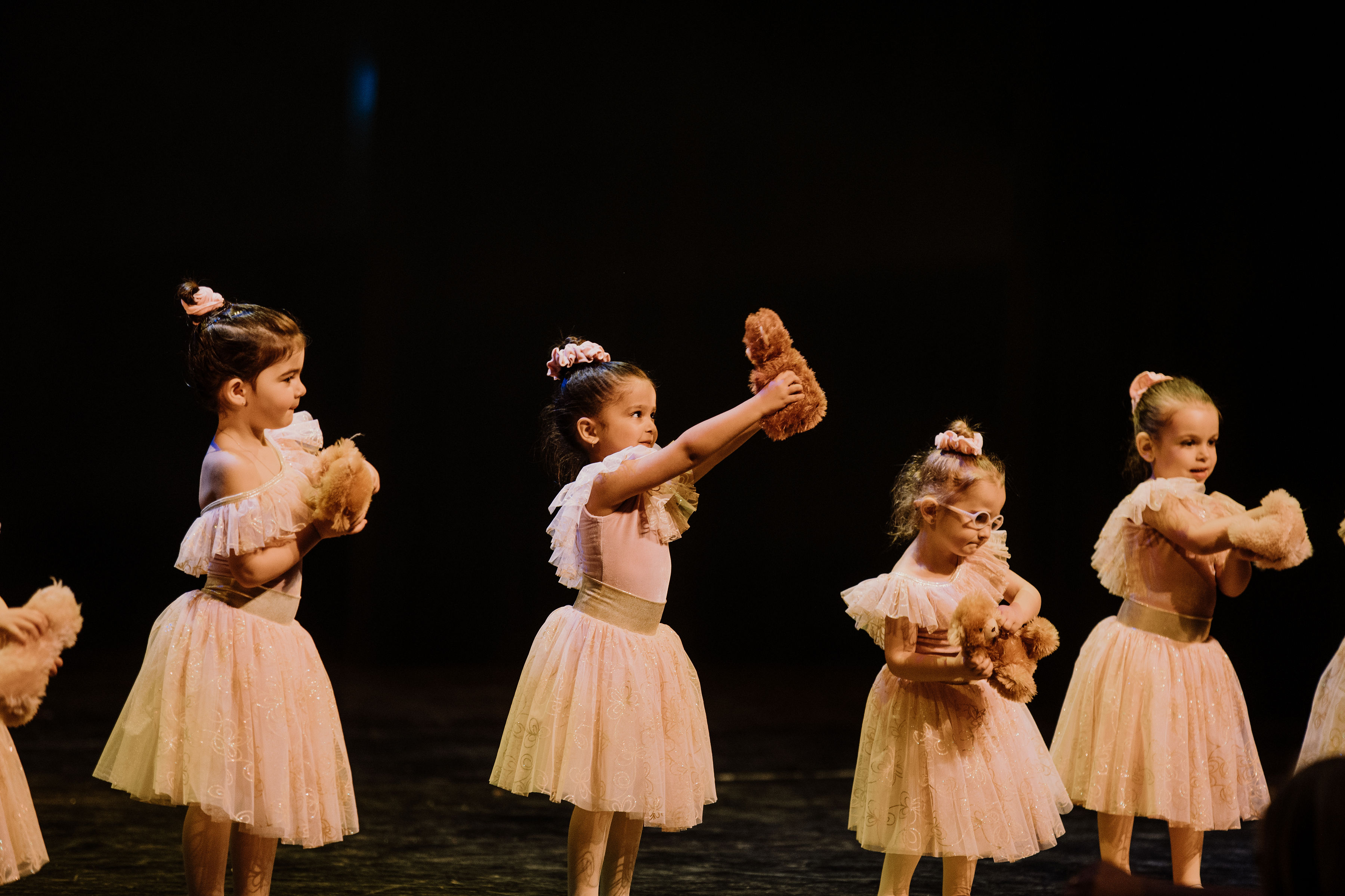 Four dancers holding bears during a ballet routine on stage