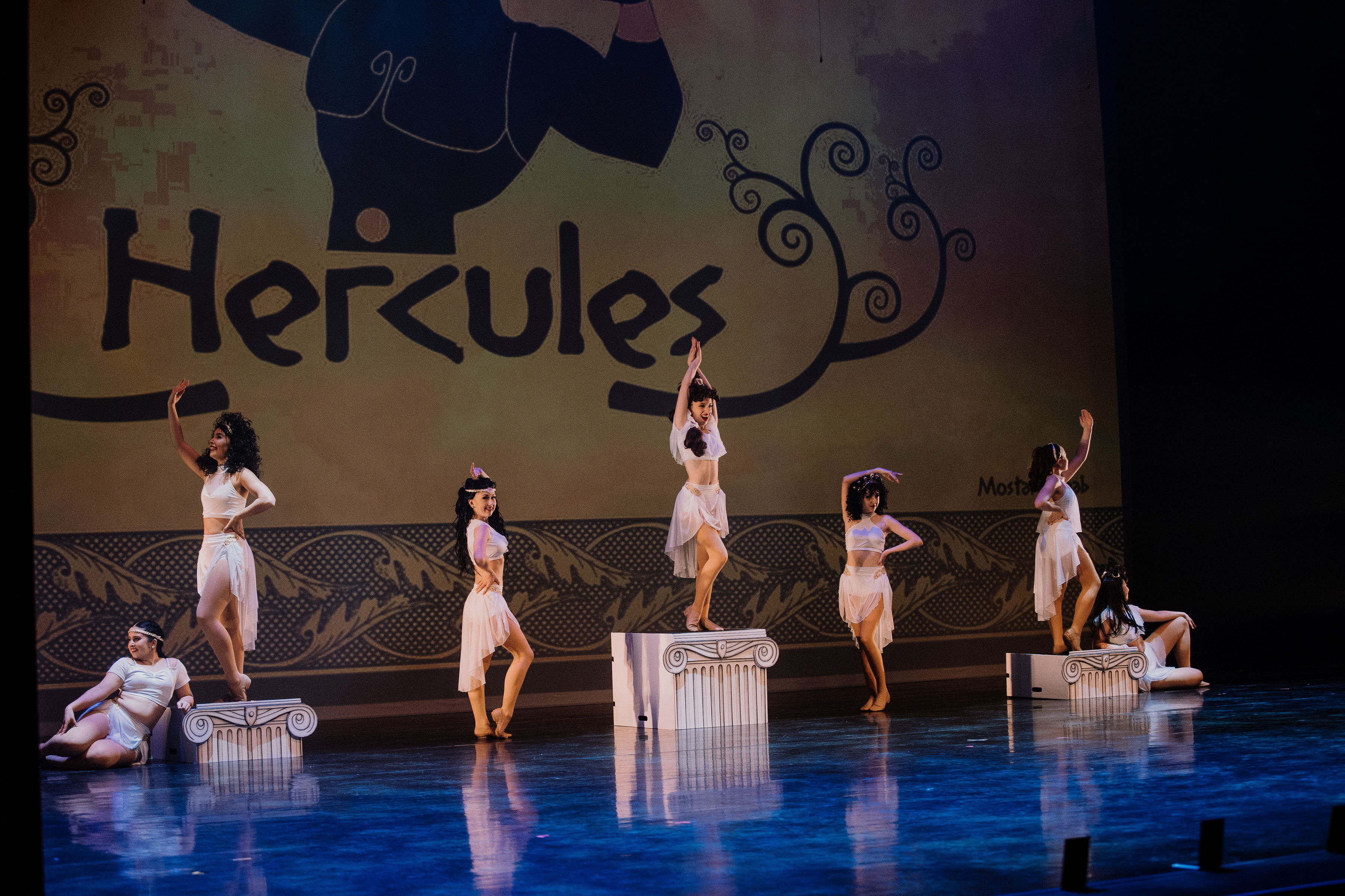 Seven dancers performing musical theatre routine on stage