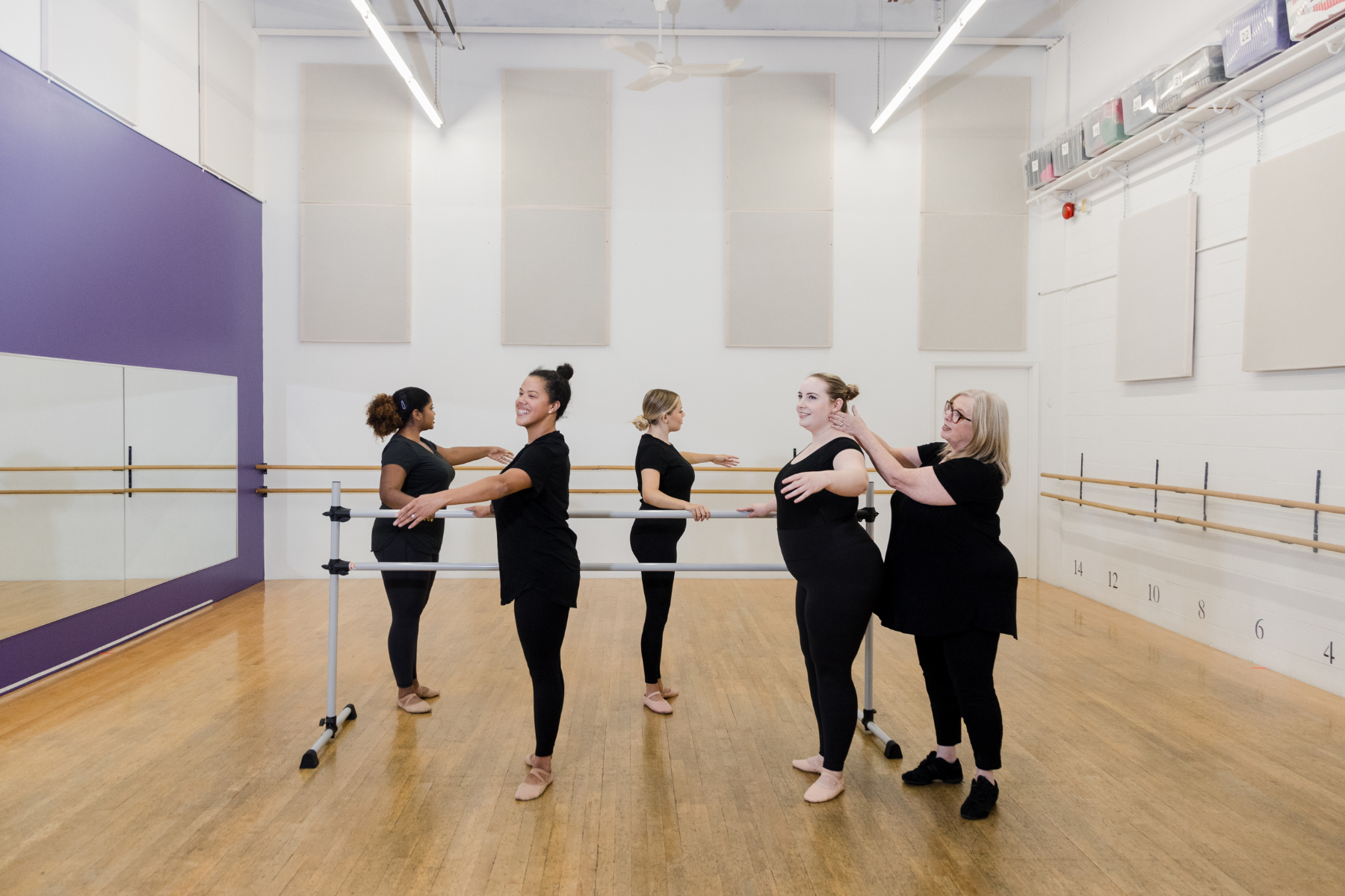 Four dancers at centre barre with Mrs. Lawrence helping with placement